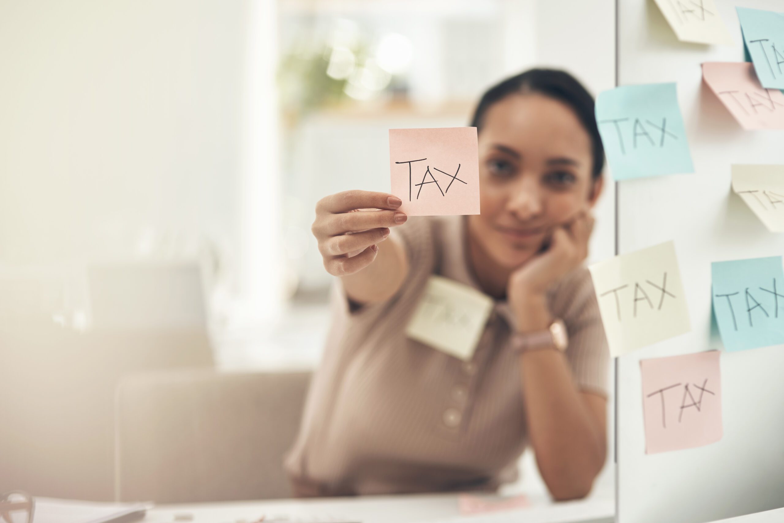 Shot of a young businesswoman holding a note with tax written on it in an office.